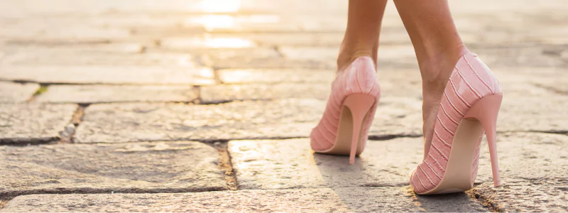Glamorous Trends of High Heels 2 A person walking on a sidewalk in high pink stiletto heels with a fabric finish and shiny heels.