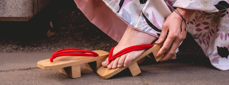 A Japanese woman in kimono trying on traditional elevated sandals made of bamboo.