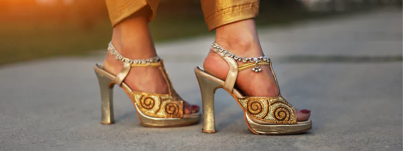 Custom-Made High Heels: Final Perfection 5 An elegant person wearing designer gold sandals with high stiletto heels, featuring shimmering golden swirl motifs.