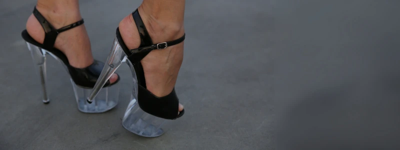 Legs in black stiletto heels with a transparent platform, standing on asphalt.