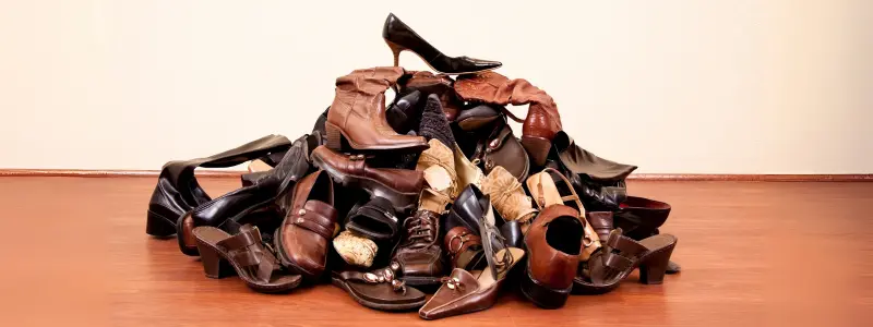 A large pile of heeled shoes in various styles, with a classic black stiletto on top.