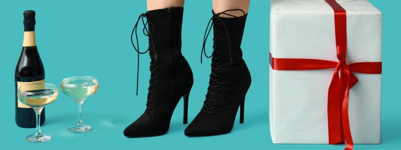 Pair of black lace‑up ankle boots with high stiletto heels worn by a person standing against a turquoise background.