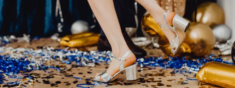 Silver block-heel party shoes worn by a man dancing among confetti and balloons, showcasing fashionable high heels for men at a festive event.